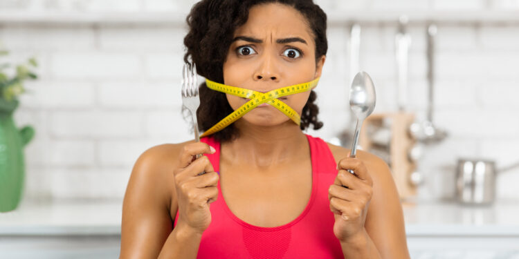 Losing Weight Concept. Close up portrait of african woman with yellow measuring tape around her mouth and wide open eyes