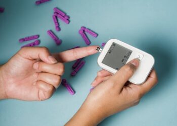 From above of crop anonymous female diabetic using electronic tool for controlling blood sugar above lancets