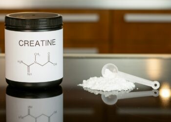 a bottle of creatine next to a spoon on a table