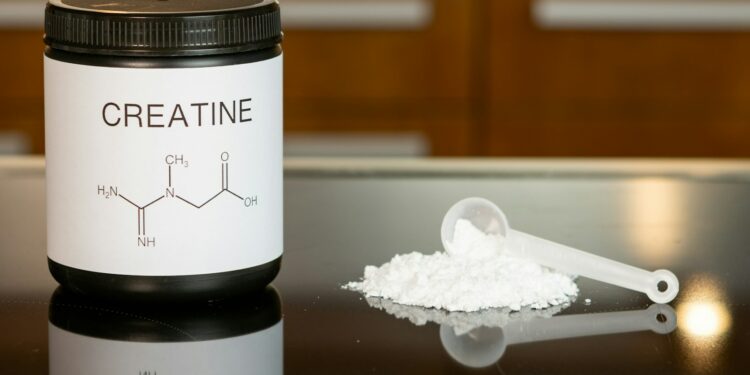 a bottle of creatine next to a spoon on a table