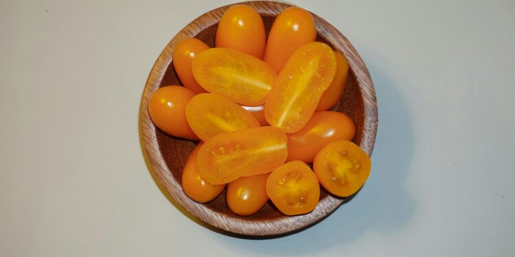 a wooden bowl filled with lots of orange tomatoes