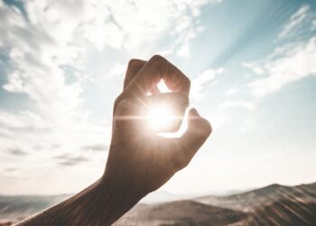 photography of sun glaring through the hole of finger