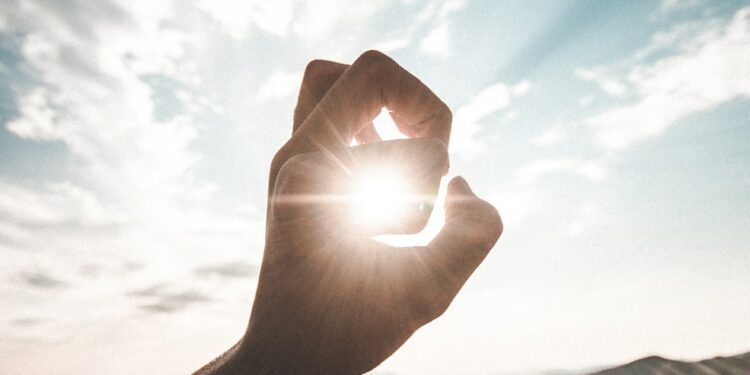 photography of sun glaring through the hole of finger