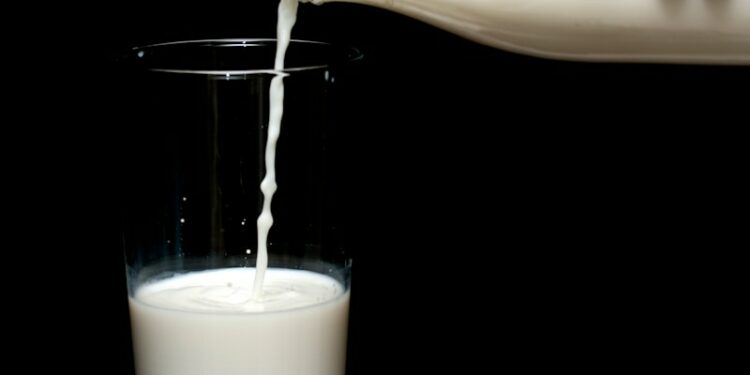 person pouring milk on clear drinking glass