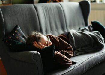 woman in pink jacket lying on gray couch