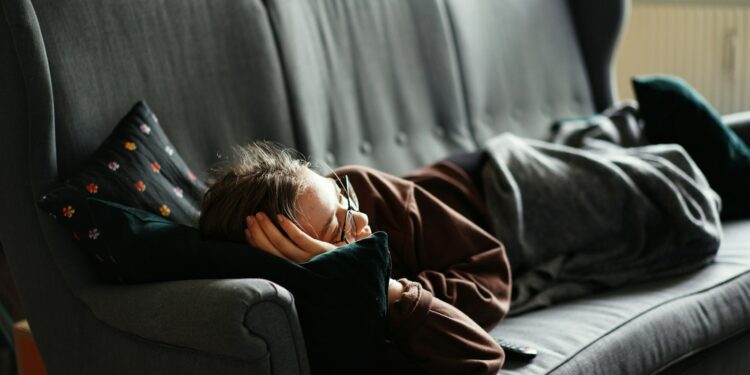 woman in pink jacket lying on gray couch