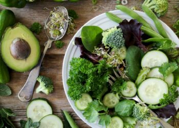 sliced broccoli and cucumber on plate with gray stainless steel fork near green bell pepper, snowpea, and avocado fruit