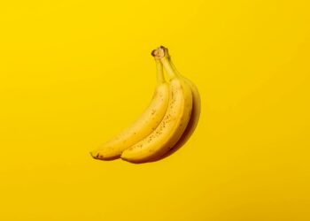 A bunch of ripe yellow bananas against a vivid yellow backdrop, offering tropical freshness.