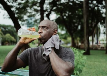Adult man drinking sports beverage and wiping sweat in a park.