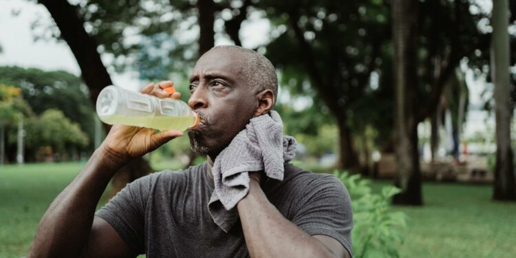Adult man drinking sports beverage and wiping sweat in a park.