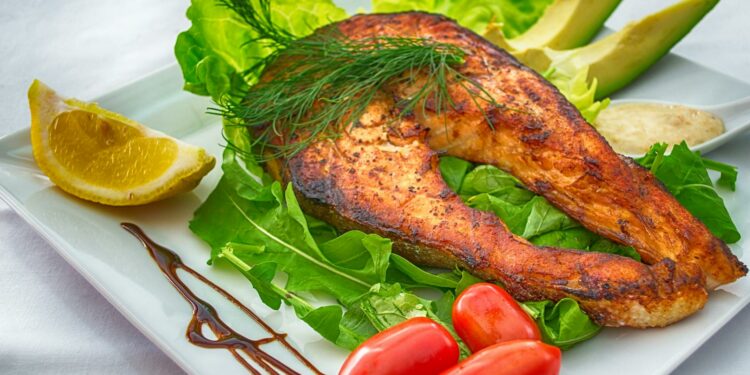Delicious grilled salmon served with fresh vegetables and herbs on a white plate.