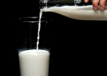 person pouring milk on clear drinking glass