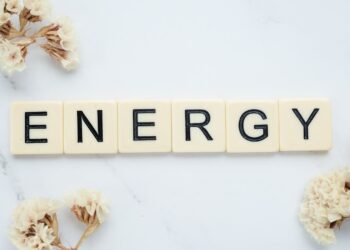 Close-up of 'Energy' spelled with Scrabble tiles on a marble surface with delicate white flowers.