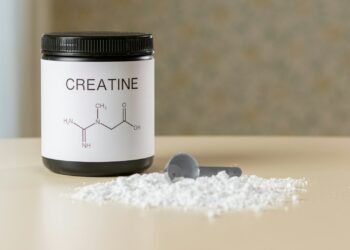 a bottle of creatine next to a spoon on a table